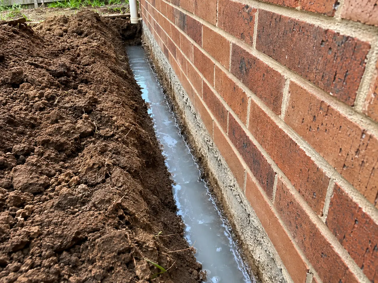A trench dug along the footing of a brick home and flooded with liquid termite barrier